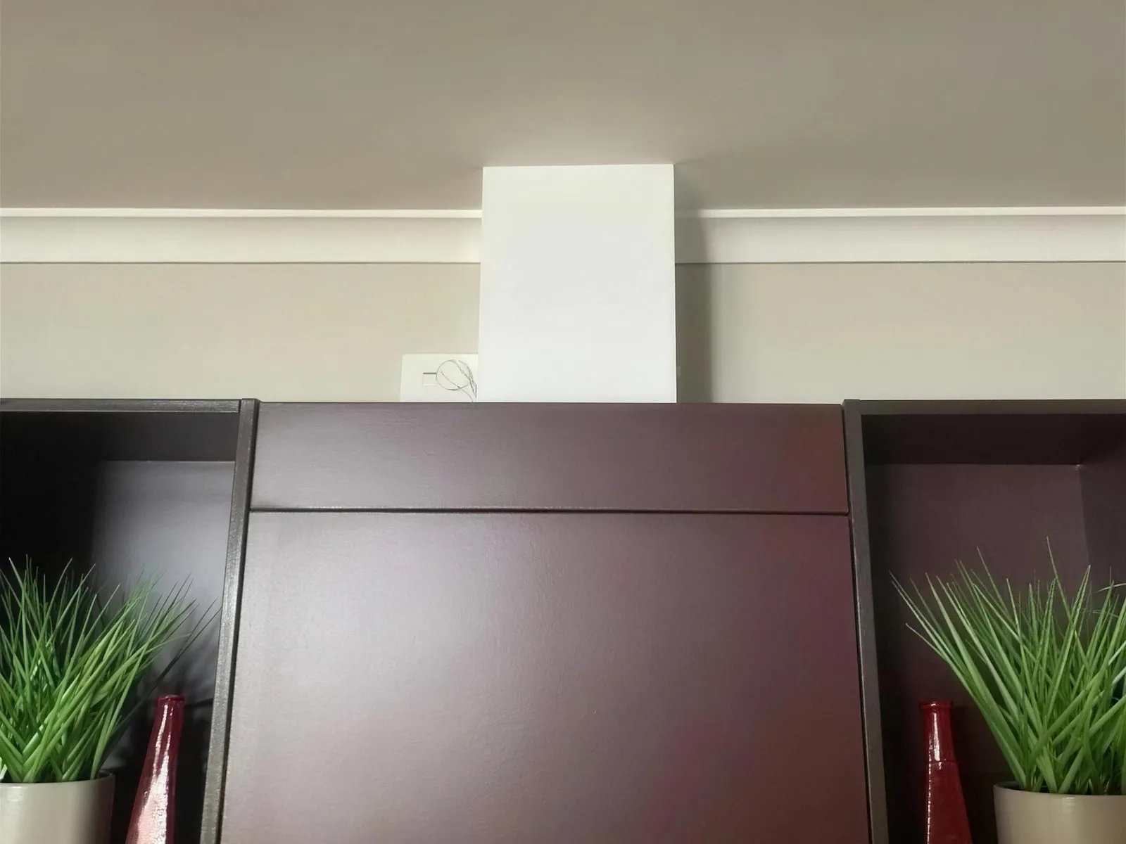 A white rangehood duct cover rising from a dark red kitchen cabinet to the ceiling.
