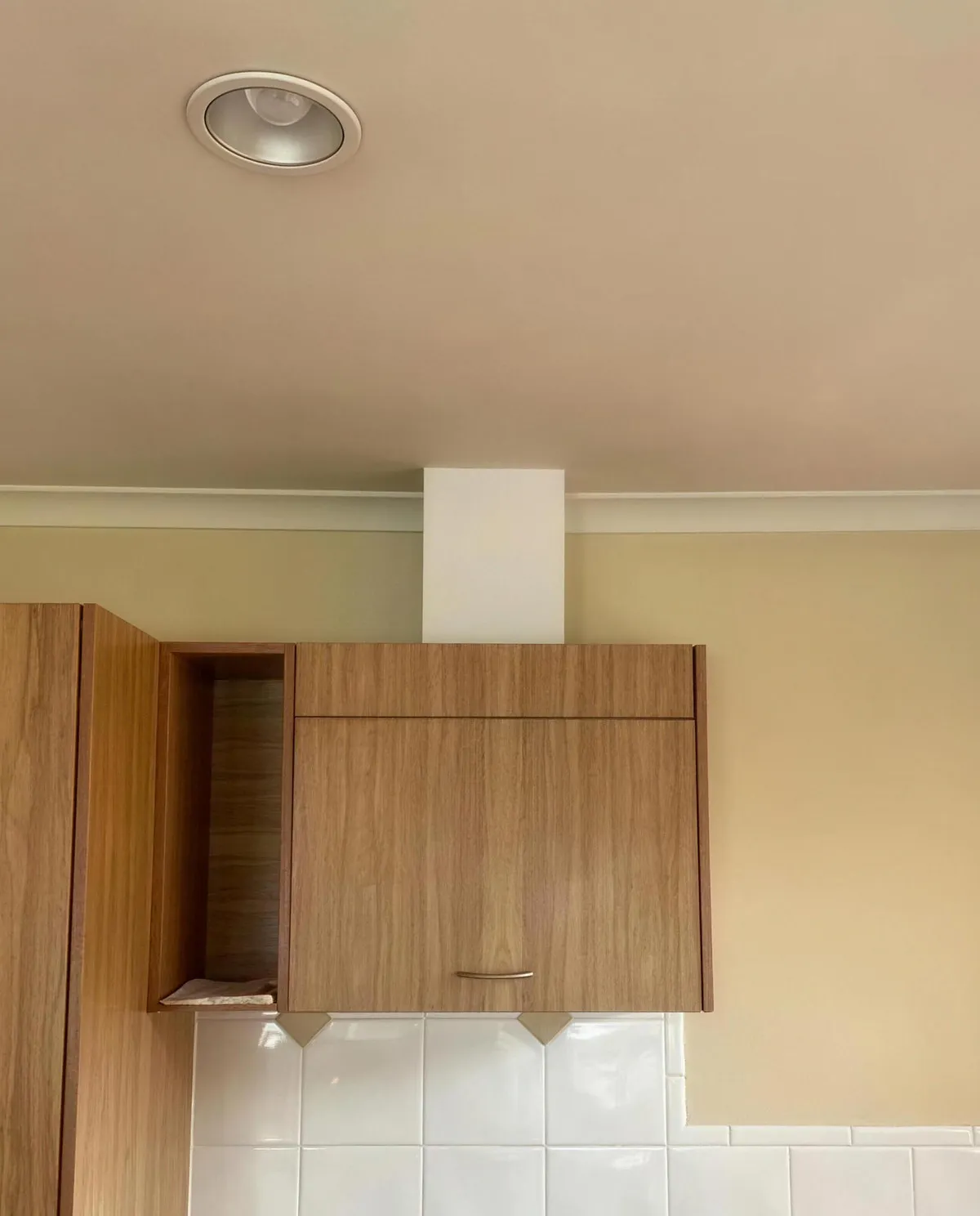 A white rangehood duct cover rising from a timber kitchen cabinet to the ceiling.